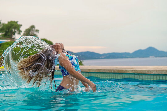 ni&ntilde;a rubia en alberca frente al mar en la playa con su cabello volando mojado disfrutando de la vida y de unas divertidas vacaciones al aire libre en la naturaleza con el agua de la alberca salpicando