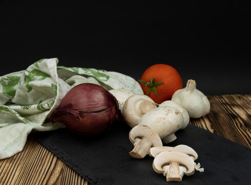Fresh mushrooms, red onion, tomato, and garlic on a slate board