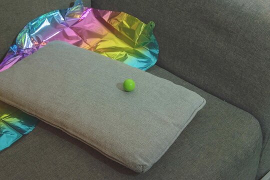 Green ball resting on a cushion beside colorful reflective sheets on a couch