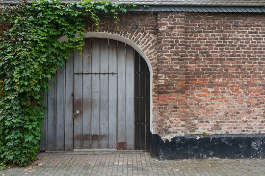 An arched wooden gate sits beneath ivy beside an aged brick wall in historic Zons, Germany