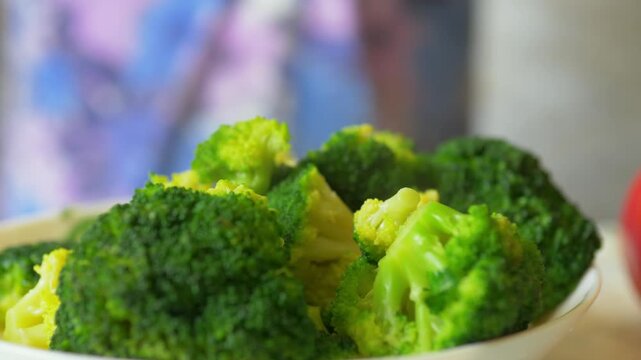 Steamed broccoli florets being drained and served into a bowl with a slotted spoon