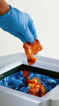 Blue gloved hand dropping crumpled candy wrapper into recycling bin with clean wall copy space