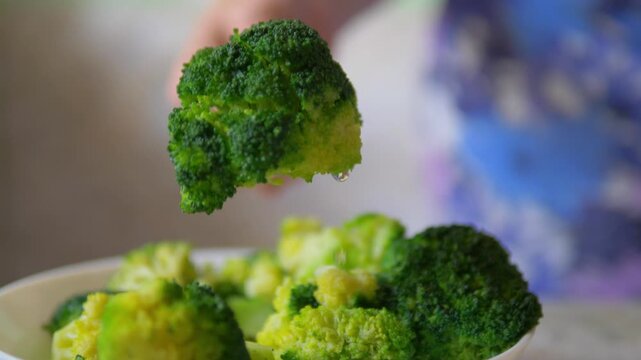 Steamed broccoli florets in a white bowl being pierced by a metal fork