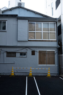 窓が段ボールや板で塞がれた古い空き家と手前の駐車場、東京の下町風景