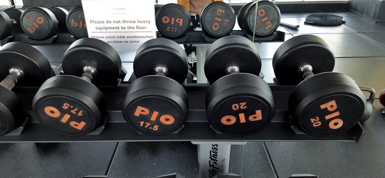 Jakarta, Indonesia - November 22 2024. Set of Round Rubber Dumbbells Arranged on Weight Rack in Gym