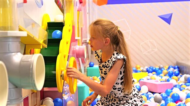 Curious child playing with interactive ball machine and colorful plastic balls at children entertainment center