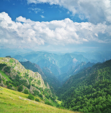Vast mountain canyon winds between steep rocky cliffs under grand white cumulus clouds and blue sky. Majestic alpine valley