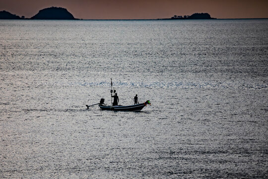 A traditional long‑tailed boat with fishermen near a tropical shore at sunset in Thailand