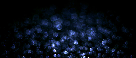 Naklejka premium Abstract blue bokeh lights on black background. Glowing blurred festive circles and holiday illumination banner. Christmas light texture overlay