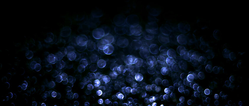 Abstract blue bokeh lights on black background. Glowing blurred festive circles and holiday illumination banner. Christmas light texture overlay