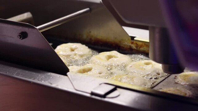 Process of frying donuts in an automatic deep fryer with oil. Close-up of a conveyor machine for making donuts. Automated production of donuts on professional equipment. Fast food production