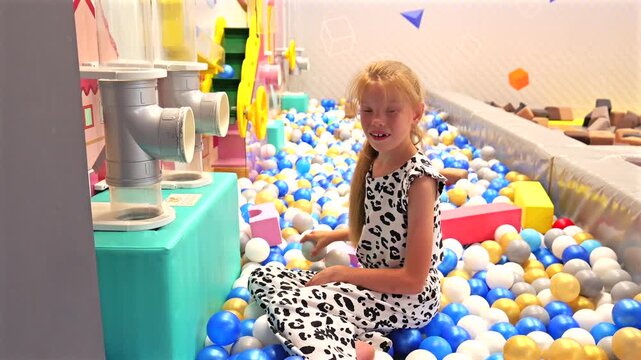 Curious child playing with interactive ball machine and colorful plastic balls at children entertainment center