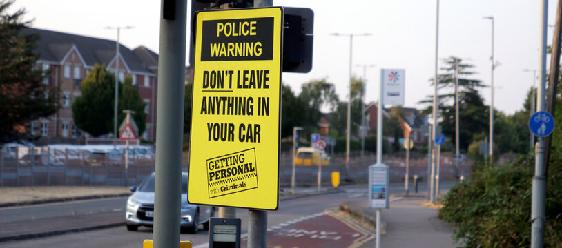 Yellow police warning sign reading don't leave anything in your car on metal pole near road for vehicle crime prevention and urban safety