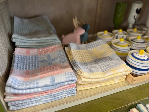 Towels neatly stacked on wooden shelf with ceramic jars and bunny figurine in cozy kitchen setting