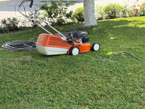 Lawn mower on green grass in garden with hose on the ground, ideal for background use