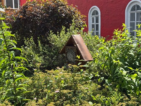 Garden landscape featuring insect house surrounded by lush greenery and red brick building background