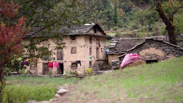 Traditional multi story mud and stone house with colorful laundry hanging beside hay stacks in Himalayan village yard