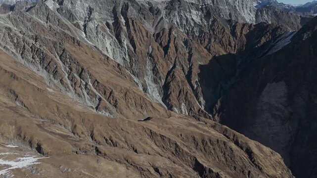 Aerial view of rugged barren Himalayan mountainside with deep ravines and scattered snow patches near Bajhang peaks
