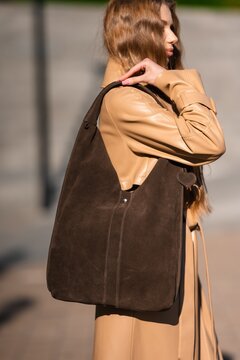 woman carrying brown suede bag walking in casual urban setting with tan leather jacket side view from behind natural light clean background copy space editorial use.