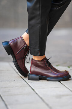 person wearing burgundy boots standing on urban sidewalk close-up of feet casual street style fashion commercial natural light clean background copy space editorial educational visual story.