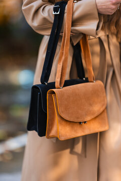 person carrying handbags in beige coat against outdoor blurred background. neutral mood, close-up side view of fashion accessories in natural light. for editorial or web.