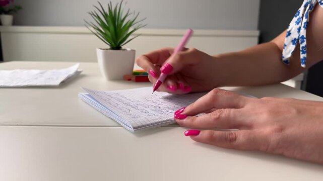 Right hand writes notes with pink striped pen while left hand steadies small squared notebook on white desk, subsequent frames show pen repositioning and page turning, with writing, hand, notebook