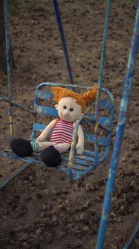 Vertical Shot of a Plush Girl Doll Swinging on Old Weathered Playground Swings