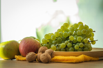 Fototapeta premium Fresh green grapes, red and green apples, and walnuts arranged on a wooden tray — perfect for healthy eating, nutrition, and organic lifestyle concepts