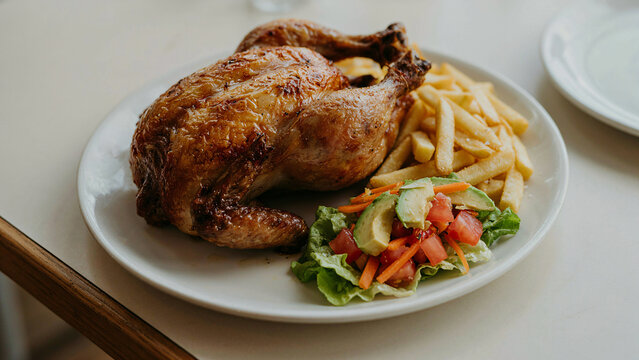 Pollo a la brasa peruano servido con papas fritas y ensalada fresca de lechuga, tomate y palta