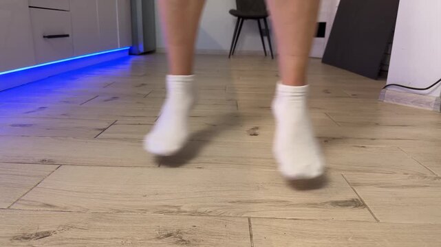 Low-angle kitchen shot of feet in white ankle socks walking on light wood plank floor with blue LED accent lighting, with sock, foot, step, movement detail, showing blur, hop, landing, stance context