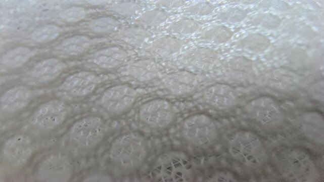 Macro close-up shot of white synthetic spacer mesh fabric. Detailed texture of breathable athletic air mesh material background, featuring a perforated honeycomb pattern and soft padded structure.