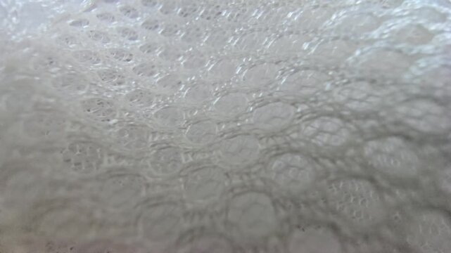 Macro close-up shot of white synthetic spacer mesh fabric. Detailed texture of breathable athletic air mesh material background, featuring a perforated honeycomb pattern and soft padded structure.