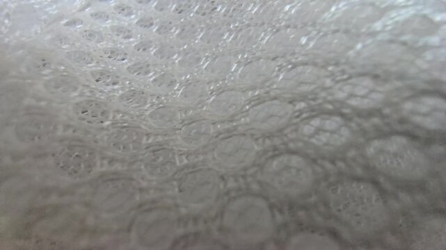 Macro close-up shot of white synthetic spacer mesh fabric. Detailed texture of breathable athletic air mesh material background, featuring a perforated honeycomb pattern and soft padded structure.