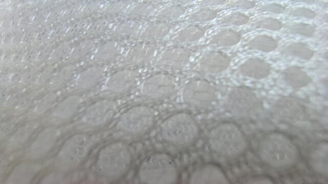 Macro close-up shot of white synthetic spacer mesh fabric. Detailed texture of breathable athletic air mesh material background, featuring a perforated honeycomb pattern and soft padded structure.