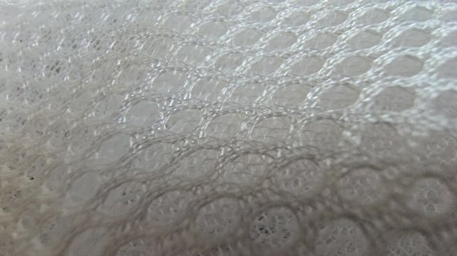 Macro close-up shot of white synthetic spacer mesh fabric. Detailed texture of breathable athletic air mesh material background, featuring a perforated honeycomb pattern and soft padded structure.
