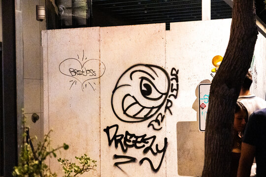 Graffiti Covered Urban Wall at Night with Tree and Passing Pedestrians