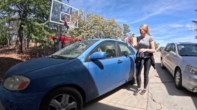 Woman leaning into blue sedan in sunlit parking lot