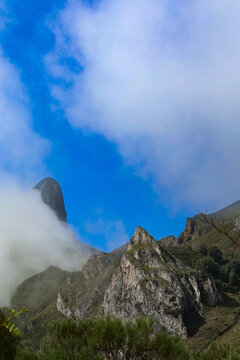 Niebla y nubes bajas rodeando picos de monta&ntilde;a calizos bajo un cielo azul despejado