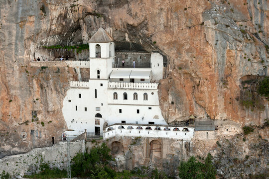 Danilovgrad, Montenegro - 26 July 2005: Aerial view of Ostrog Monastery built into the vertical rock face, featuring white stone walls, arched windows, and a bell tower.