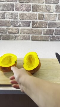Close-up food preparation b-roll video showing a chef moving a parchment-covered baking sheet into frame behind fresh halved Hokkaido pumpkin on a cutting board against a brick wall.