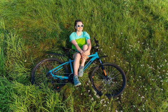 Young woman sitting on blue bicycle in green field, enjoying calm outdoor leisure and summer sunshine
