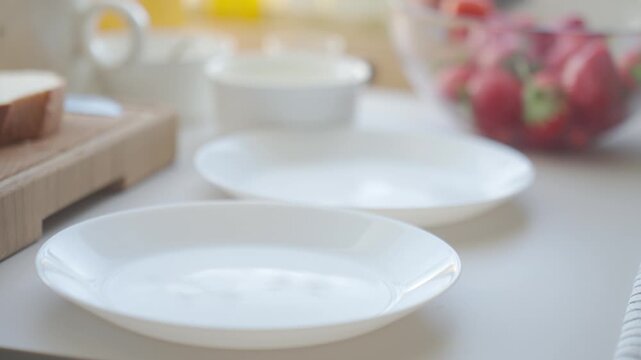 Hand sets plates on a table and places French toast slices onto them. Concept of homemade breakfast and serving food