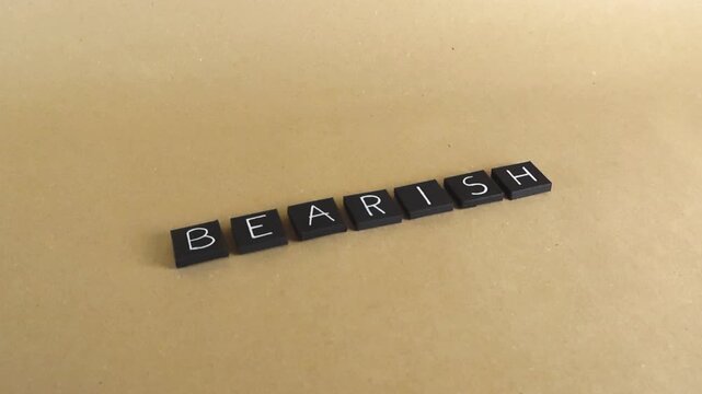 Sliding shot of the word bearish spelled out with black letter tiles on a brown paper background, symbolizing a pessimistic market trend, falling prices, and economic downturn