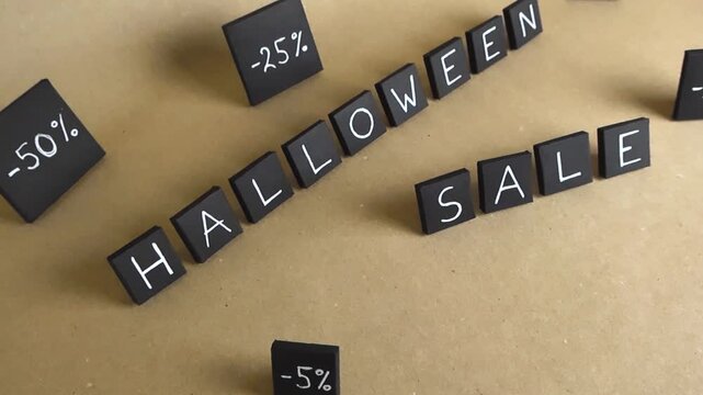 Black tiles with the inscription Halloween Sale moving on a craft paper background, surrounded by various percentage discounts for a special promotional offer during the autumn holiday season