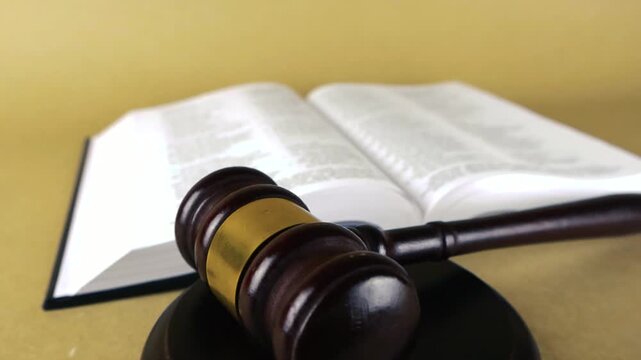 Wooden judge's gavel and sound block resting on the pages of an open Holy Bible, symbolizing the intersection of religious scripture, law, and moral judgment on a solid background