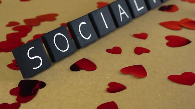 Conceptual video with the word socialism written on black tiles, surrounded by shiny red heart shaped confetti on a cardboard background, representing a positive view of the political ideology