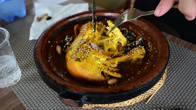 Marrakech, morocco. August 8, 2026. A person uses a knife and fork to eat a delicious chicken tagine with prunes, almonds, and sesame seeds in a marrakech restaurant