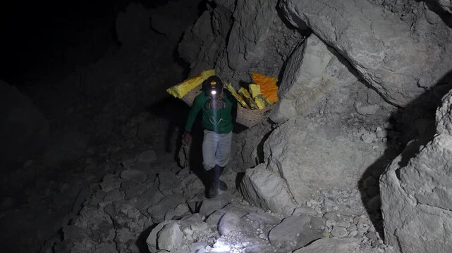 Sulfur miner lifts heavy sulfur baskets inside Kawah Ijen crater.