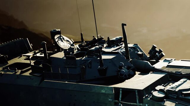 A military vehicle sits on rocky ground as the sun sets in the background. The scene shows details of the vehicles exterior features and equipment.