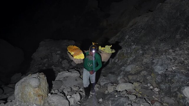 Working sulfur miner carrying heavy load from Kawah Ijen crater in East Java, Indonesia, showcasing traditional manual labor on the steep rocky path of the active volcano